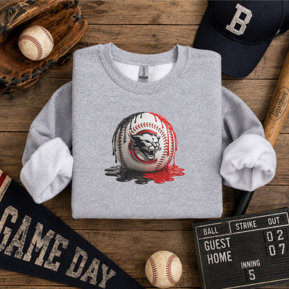 A folded heather gray long-sleeve shirt with rolled cuffs, featuring a Charleroi Cougar baseball graphic of a cougar head inside a baseball with red paint drips. The shirt is styled on a wooden background with baseball props including a cap, glove, scorecard, and balls.