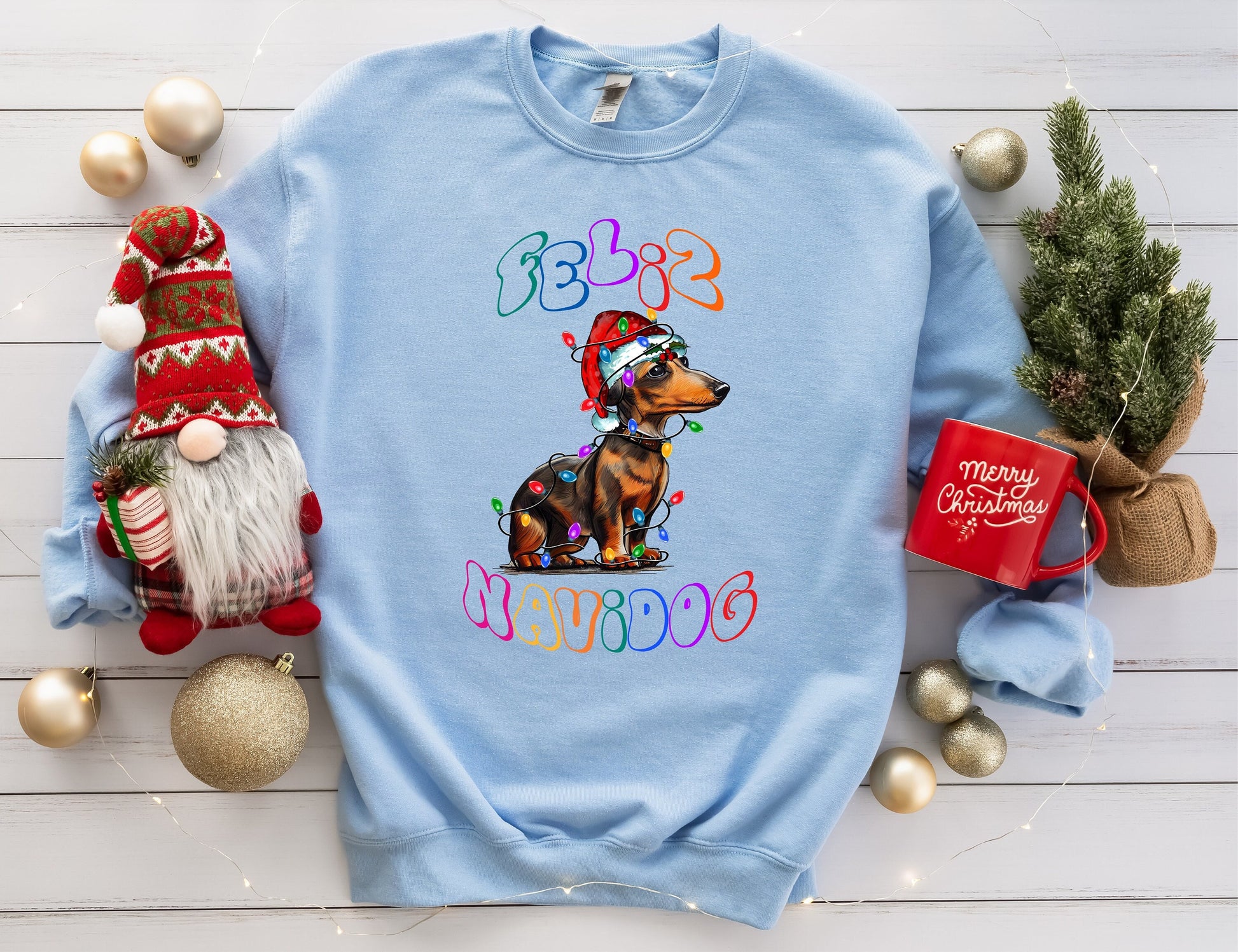 Feliz Navidog featuring an adorable dachshund wrapped in christmas lights wearing a santa hat.  Available in several colors.  T shirt and sweatshirt available.  Youth, Adult and plus sizes.