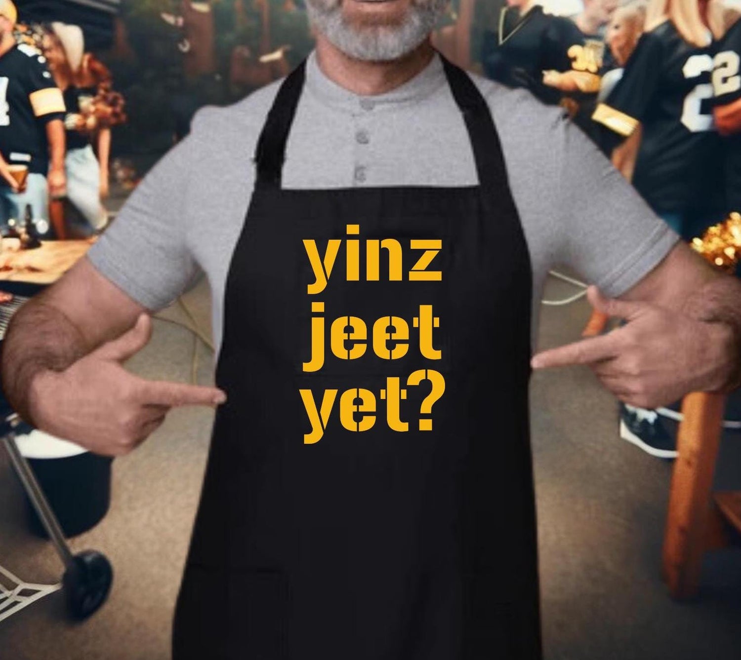 yinz jeet yet? printed in gold on a black apron with a man pointing to the apron at a tailgate party.