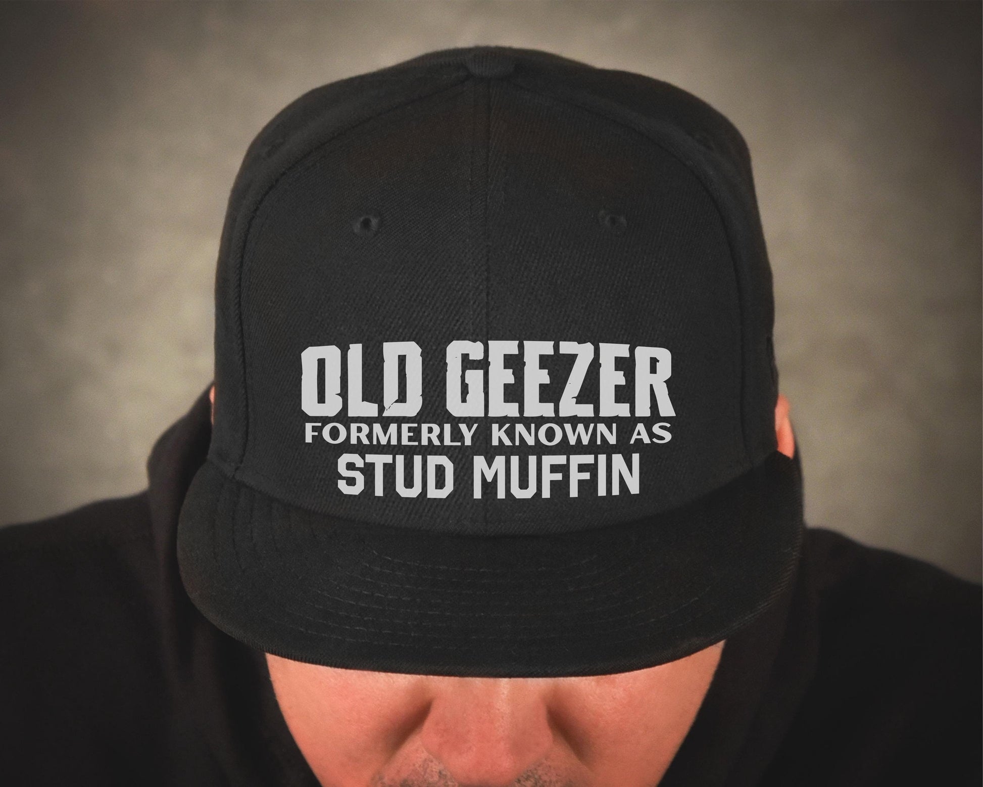 Old Geezer formerly known as Stud Muffin printed in white on a black baseball trucker hat.