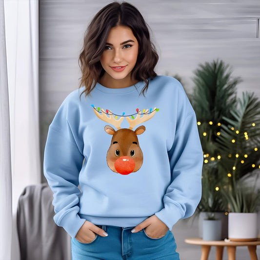 Light blue Christmas sweatshirt with a cute reindeer face, red nose, and festive holiday lights on antlers. Modeled by a woman standing indoors, adding cozy holiday vibes.