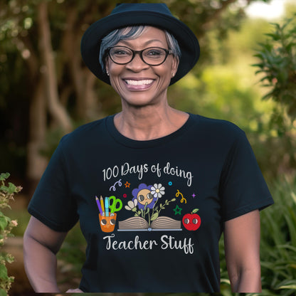 Smiling teacher wearing a black 100 Days of Doing Teacher Stuff t-shirt, featuring colorful illustrations of pencils, flowers, and an apple, perfect for celebrating the 100th Day of School.