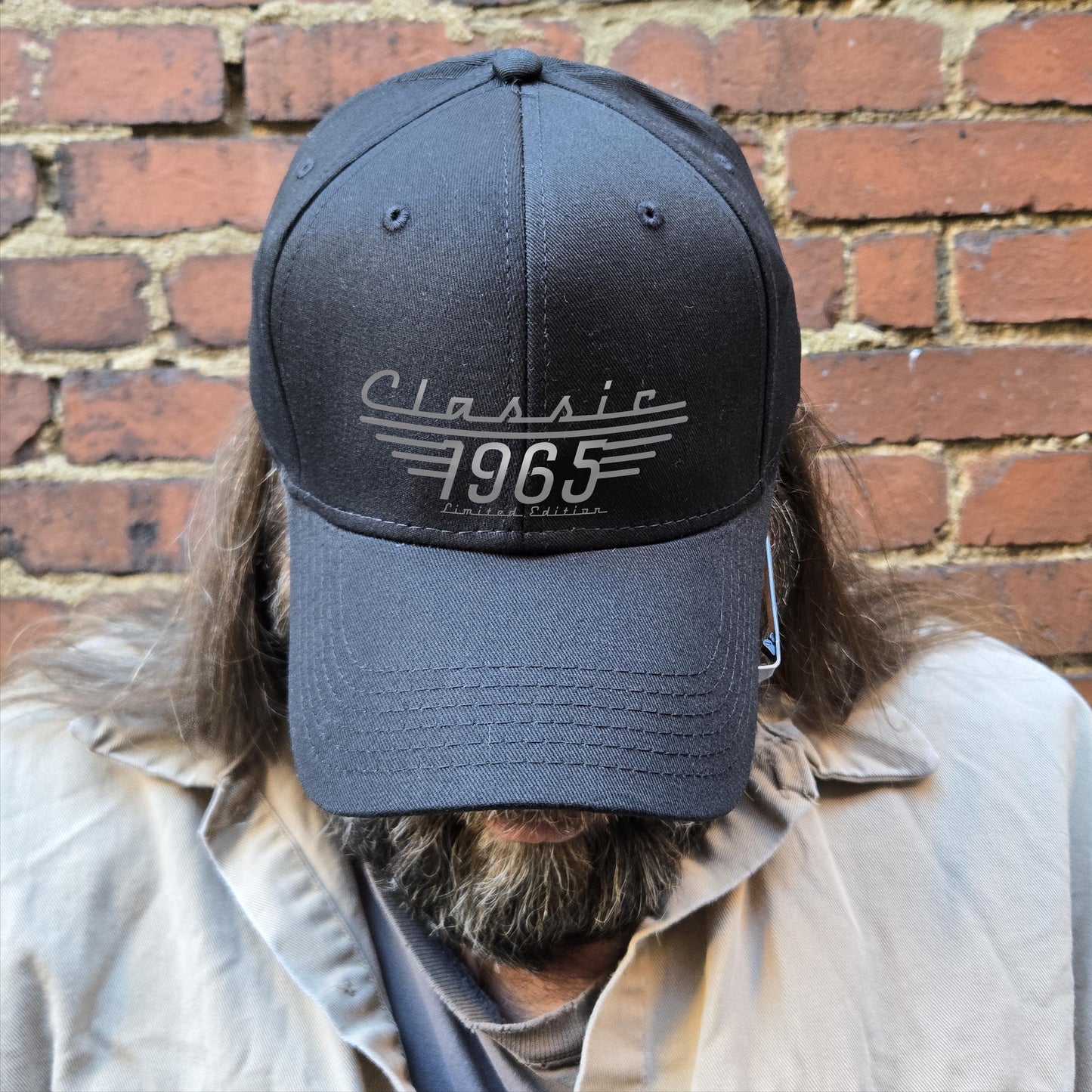 Black Classic 1965 Limited Edition baseball cap displayed on a bearded man against a brick wall.
