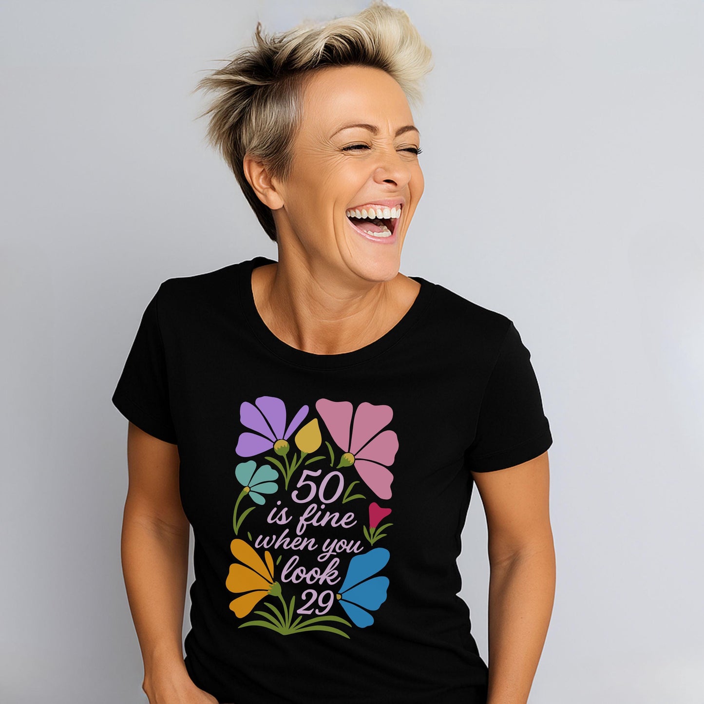 Woman wearing black tee with “50 is fine when you look 29” floral graphic, laughing joyfully.