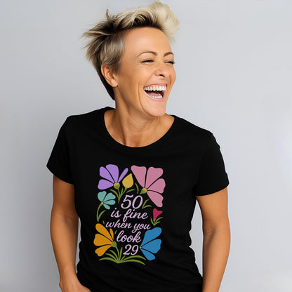 Woman wearing black tee with “50 is fine when you look 29” floral graphic, laughing joyfully.
