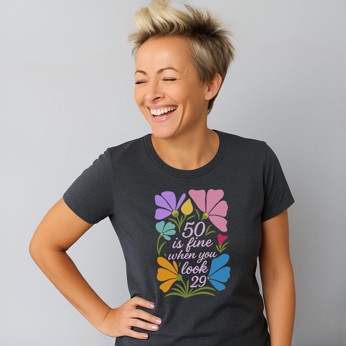 Woman wearing dark heather grey tee with colorful floral “50 is fine” design.