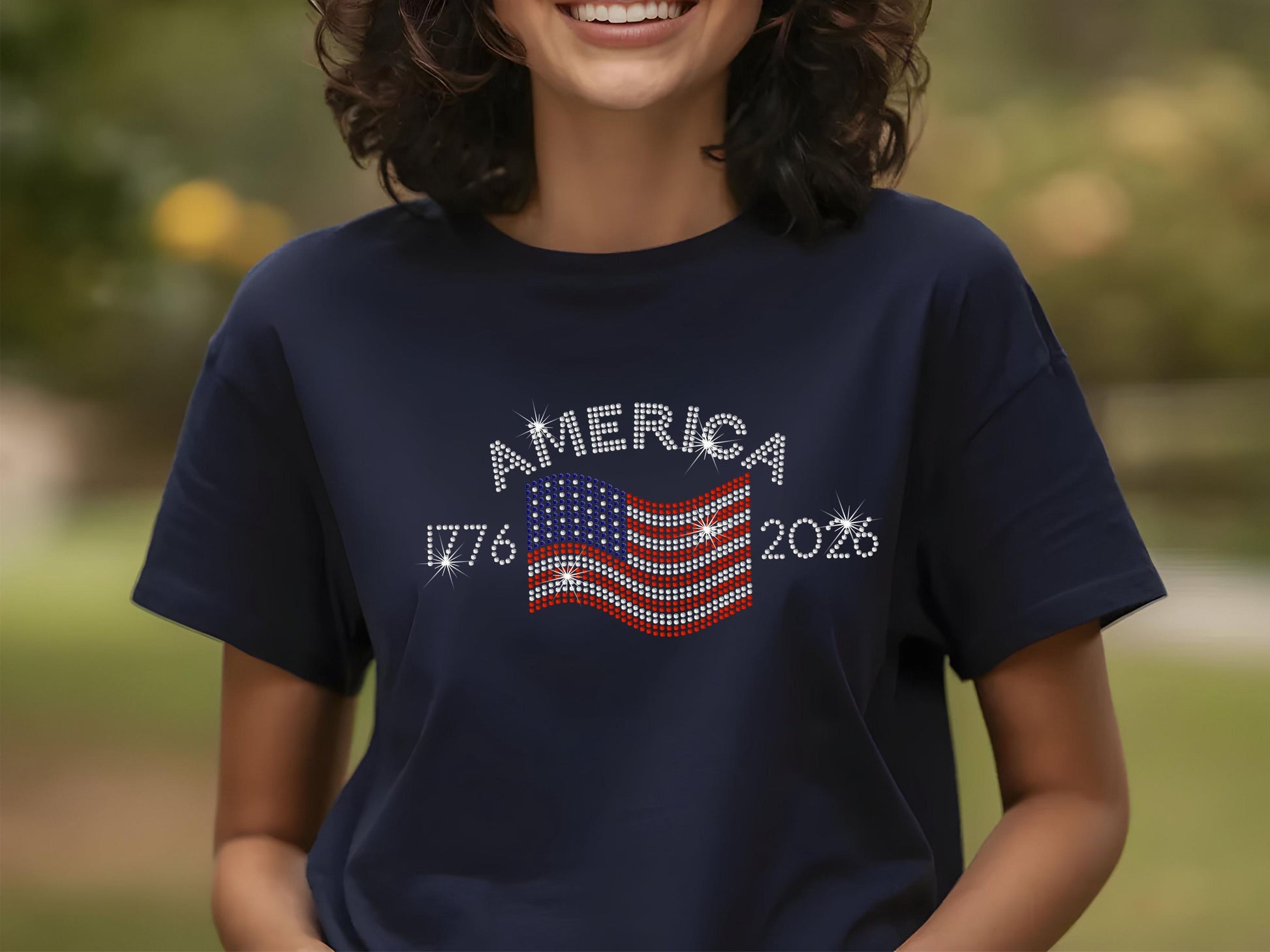 Smiling woman wearing navy t-shirt with rhinestone USA flag and America 250th anniversary design outdoors.