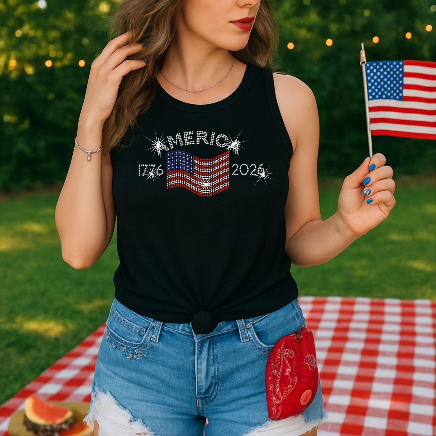 Woman at picnic holding small USA flag, wearing black Tank with a rhinestone America 1776 - 2006 design.