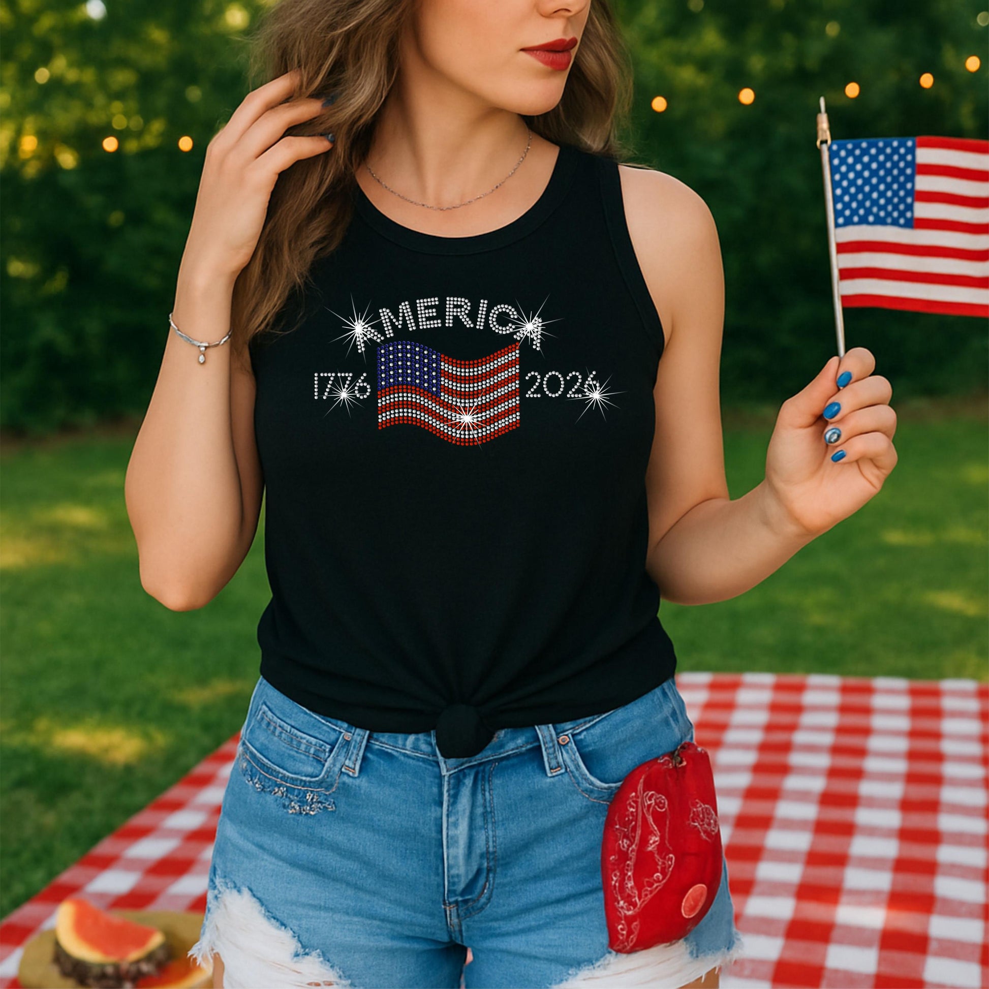 Woman at picnic holding small USA flag, wearing black Tank with a rhinestone America 1776 - 2006 design.