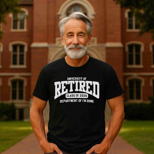 Older man with gray hair and a beard standing confidently on a college campus walkway, wearing a black t-shirt that reads “University of Retired – Class of 2026 – Department of I’m Done.” The brick academic building in the background completes the collegiate theme