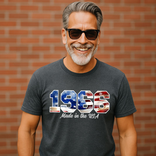 Smiling middle-aged man wearing dark heather gray t-shirt with bold red, white, and blue distressed American flag numbers reading ‘1966 Made in the USA’. Patriotic 60th birthday shirt celebrating 1966 birth year, vintage USA pride design, outdoor brick wall background. Just in time for the USA 250th