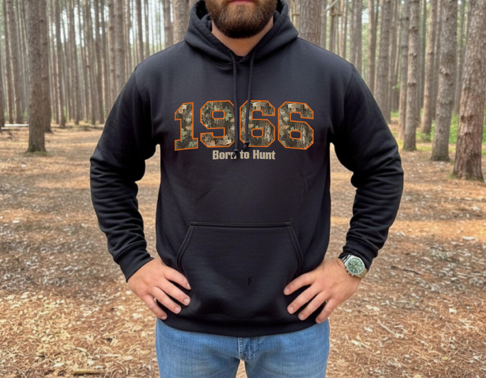 Man wearing black hunting hoodie with camouflage 1966 graphic and “Born to Hunt” text, outdoor forest setting, rugged hunting apparel.  Great gift for a hunter celebrating his/her's 60th birthday