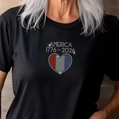 Woman wearing black rhinestone America 250th t-shirt with red, white, and blue flag heart, smiling against brick wall.