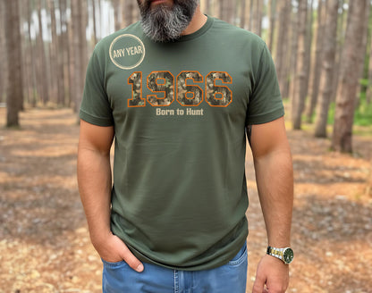 Man with grey beard wearing a 1966 Born to Hunt t-shirt with orange-outlined camouflage numbers in a pine forest. Perfect for the hunter who is turning 60 year old.