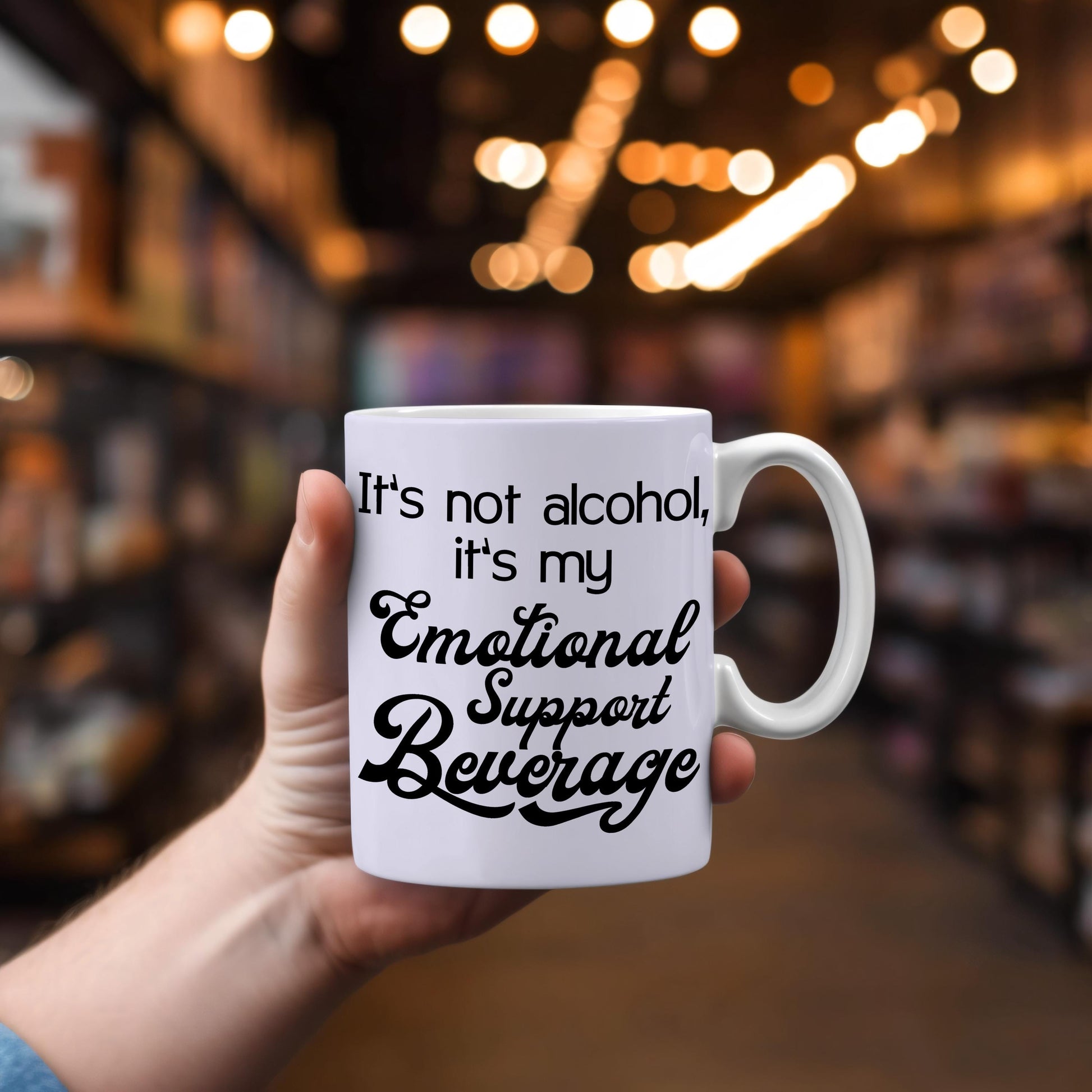 White ceramic mug with black text It's not alcohol it's my emotional support beverage held in hand