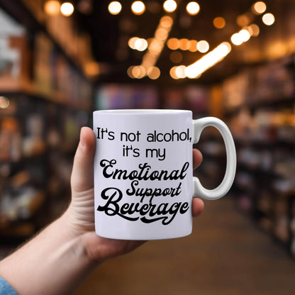 White ceramic mug with black text It's not alcohol it's my emotional support beverage held in hand