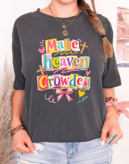 Woman wearing a comfort colors pepper t-shirt with colorful ransom letter collage text reading Make Heaven Crowded with pink bows and crosses.