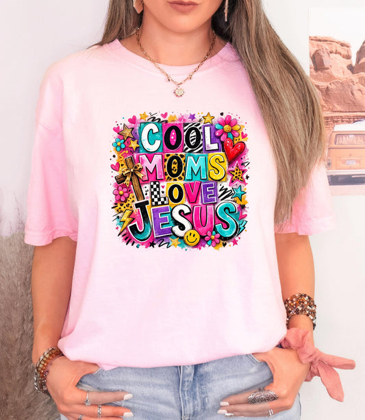 Woman wearing a colorful "Cool Moms Love Jesus" ransom note style collage graphic t-shirt in a bright, trendy collage design.