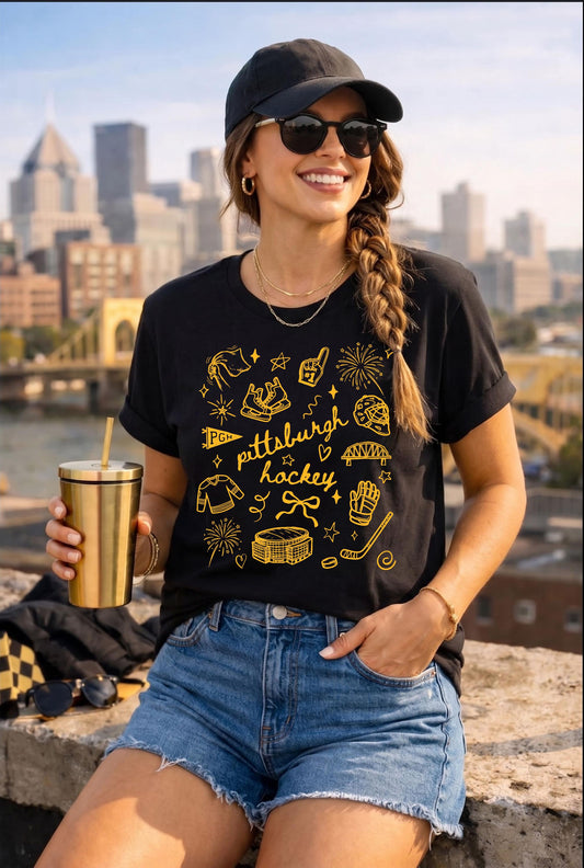 Model wearing a black Pittsburgh hockey doodle t-shirt with gold illustrations and city skyline background.